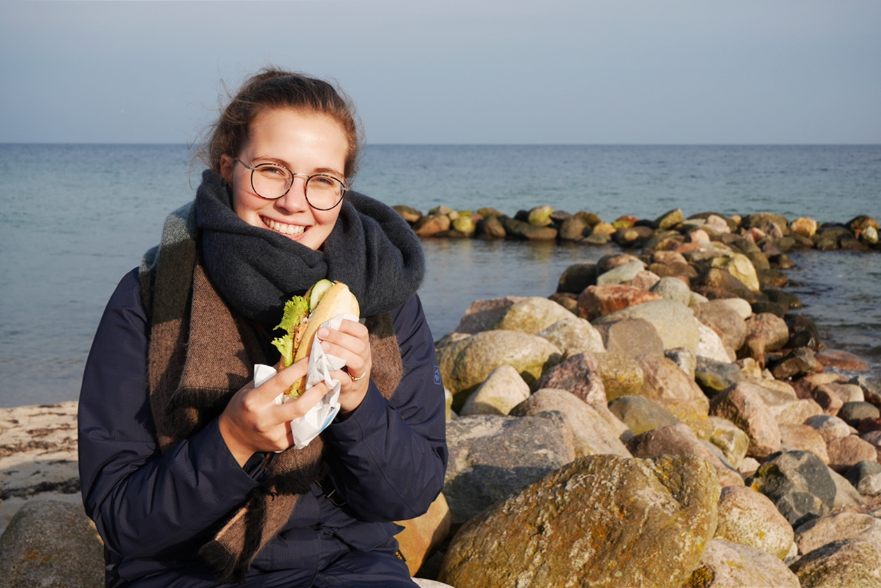 Lynn isst ein Fischbrötchen am Ostseestrand