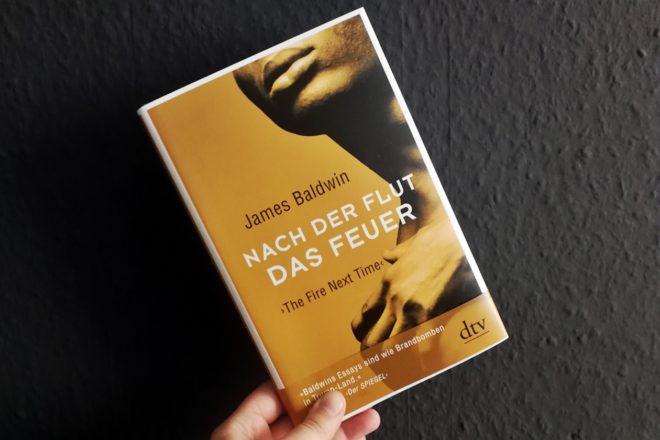 Hand mit dem Buch Nach der Flut das Feuer von James Baldwin