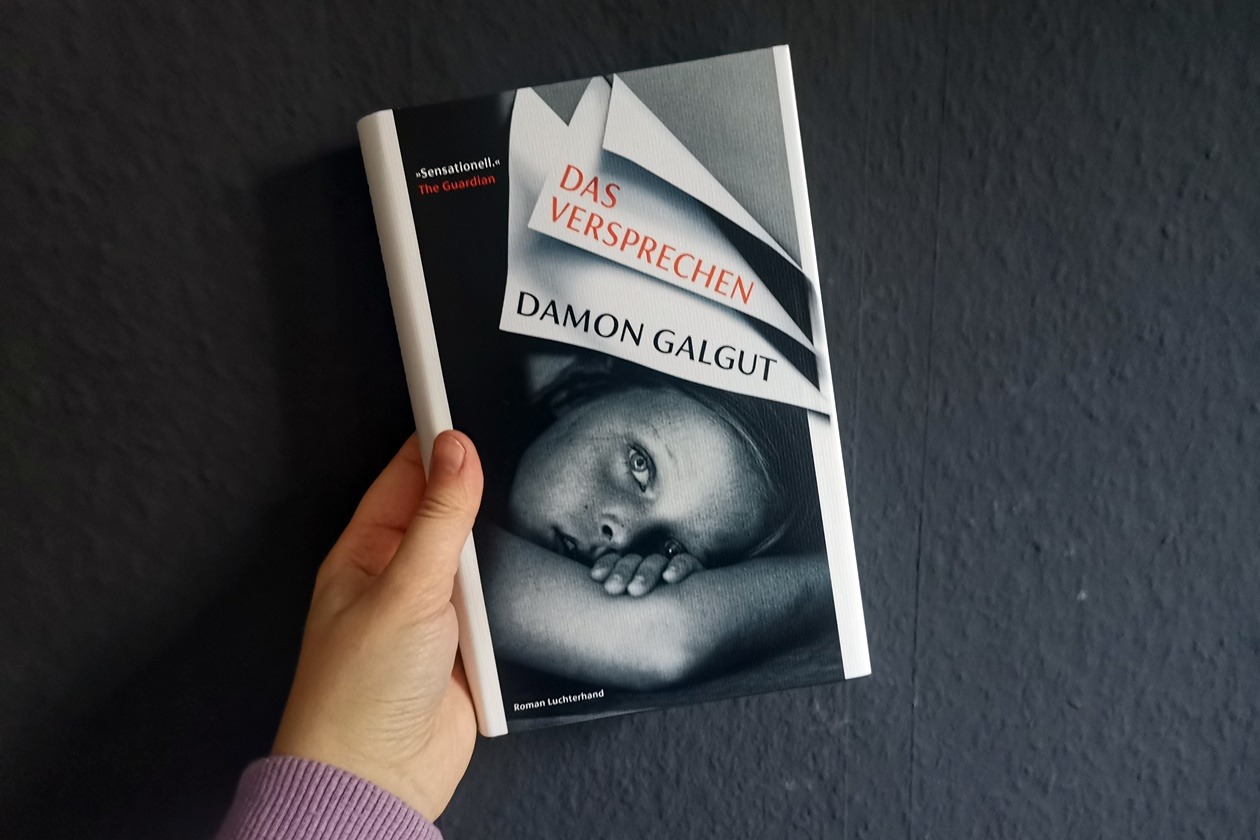 Hand die das Buch "Das Versprechen" von Damon Galgut in den Händen hält
