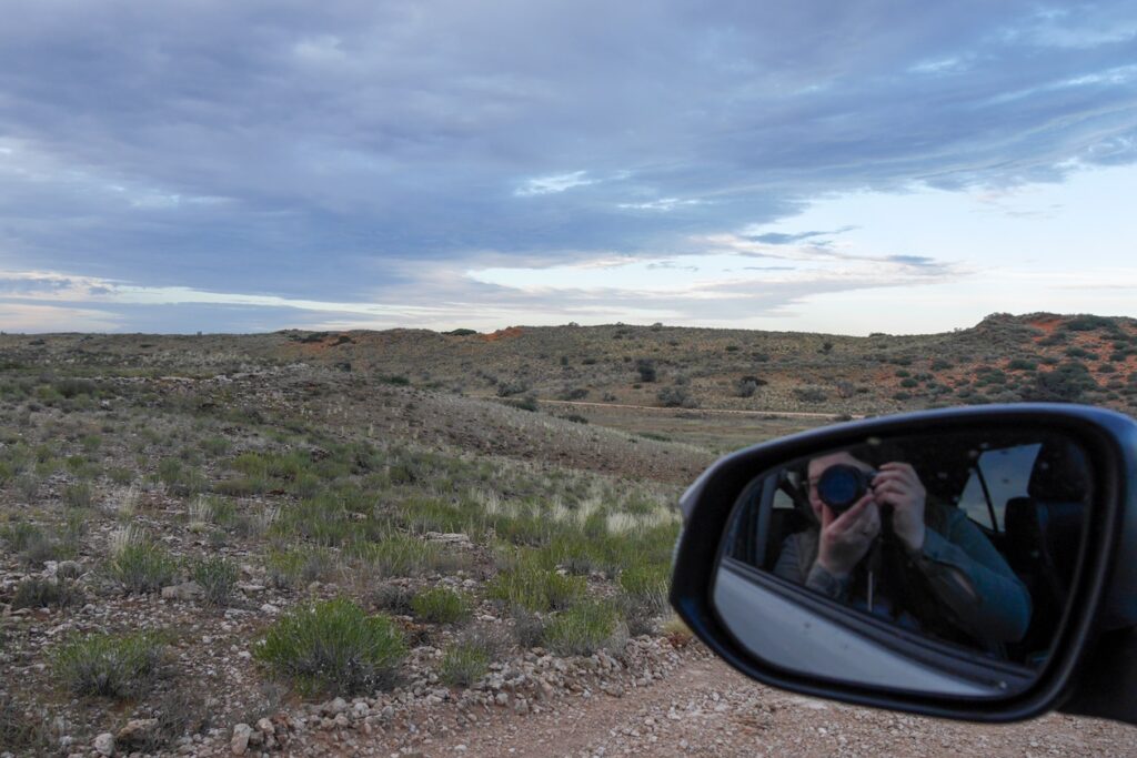 Selfie im Außenspiegel unseres Toyotas mit Blick auf die roten Dünen der Kalahari im Kgalagadi Nationalpark.