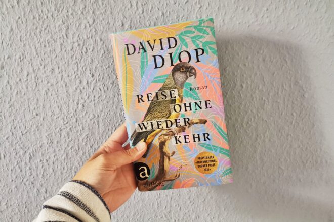 Hand, die das Buch Reise ohne Wiederkehr von David Diop gegen eine Wand hält.
