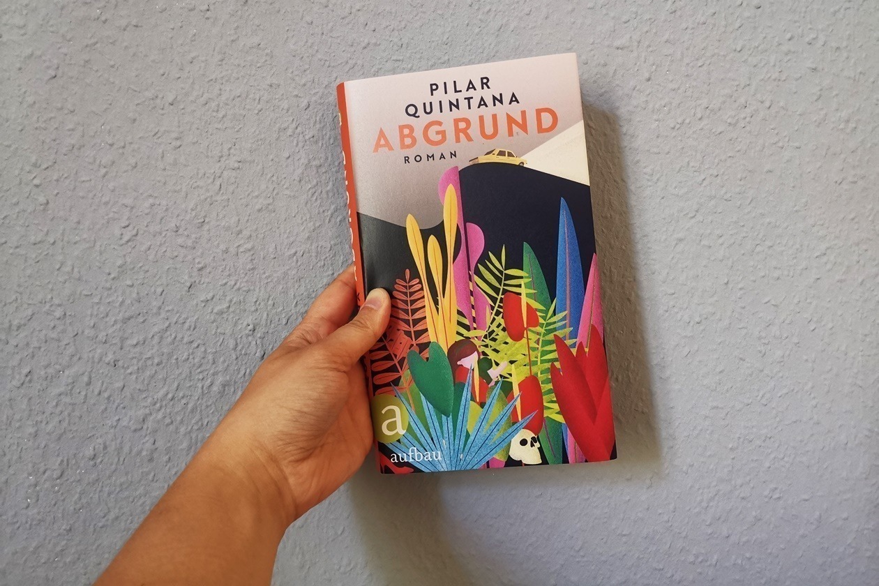 Eine Hand hält das Buch Abgrund von Pilar Quintana gegen eine hellblaue Wand