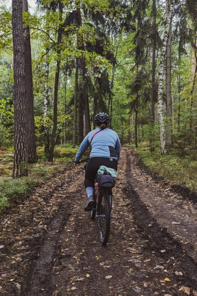 Radfahrerin von hinten, die auf einem matschigen Waldweg fährt.
