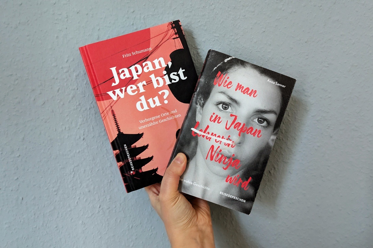 Eine Hand hält zwei Bücher über Japan gegen eine hellblaue Hand. Links "Japan, wer bist du?" und rechts "Wie man in Japan Ninja wird".