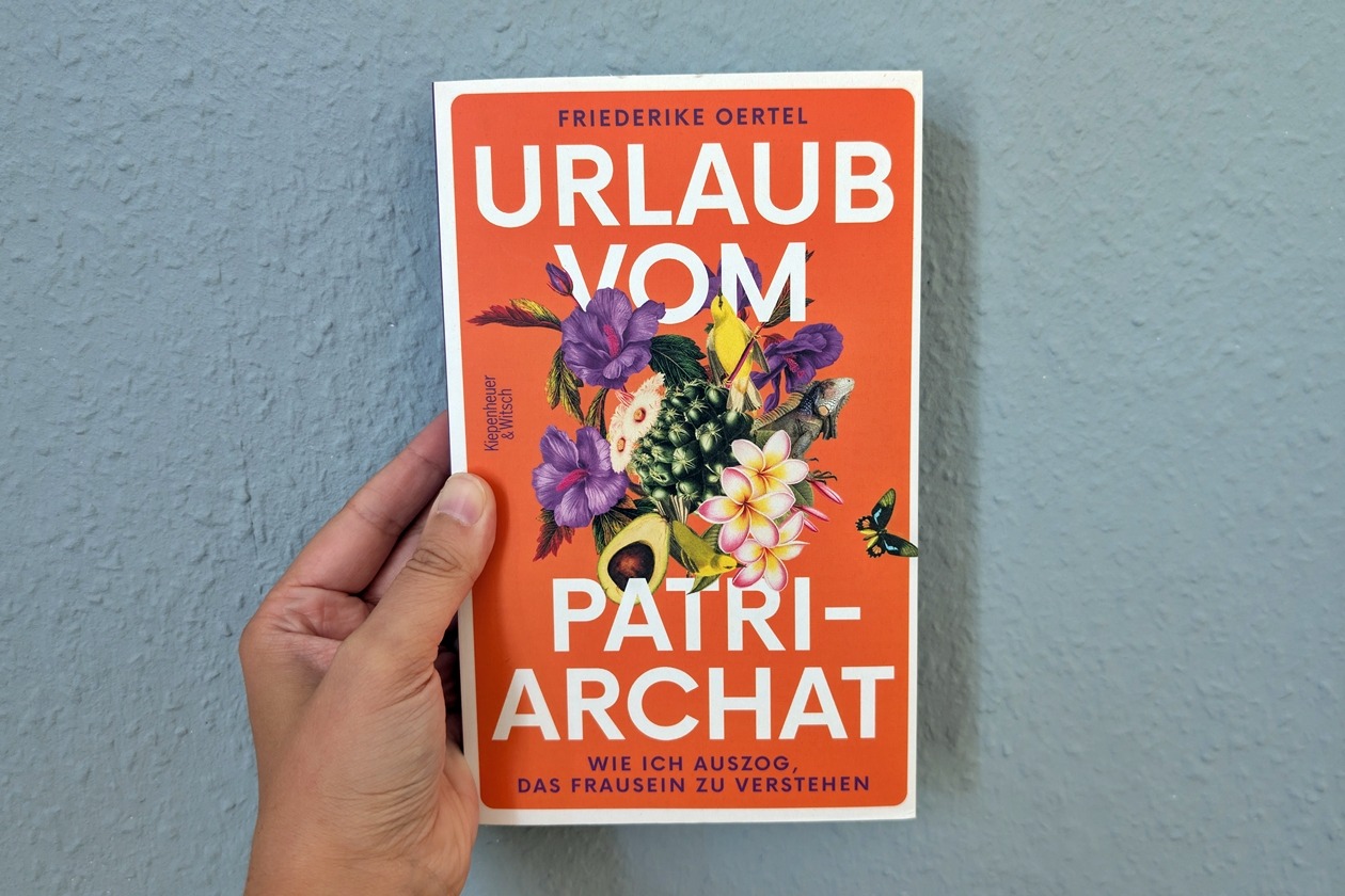 Eine Hand hält das Buch "Urlaub vom Patriarchat" von Friederike Oertel gegen eine hellblaue Wand.