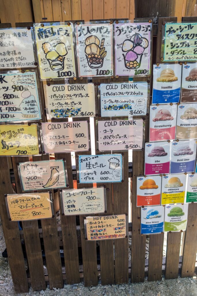 Bunte Schilder weisen auf die kulinarischen Angebote eines kleinen Cafés auf Taketomi hin.