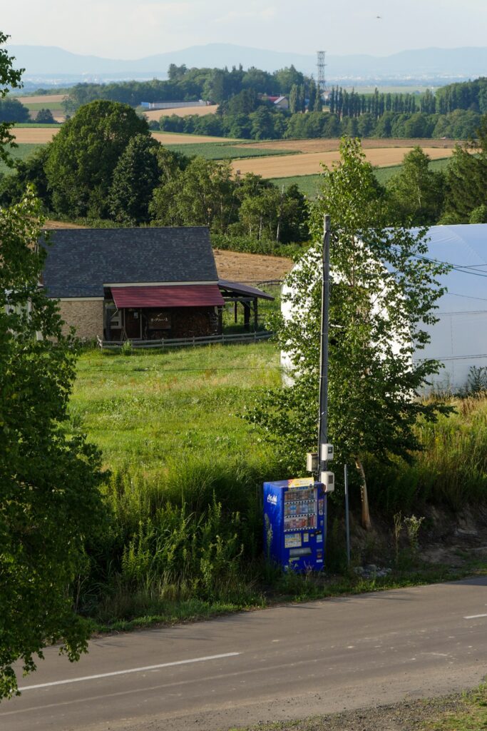 Blick auf ein Farmgebäude und eine Vending Machine im ländlichen Hokkaido.