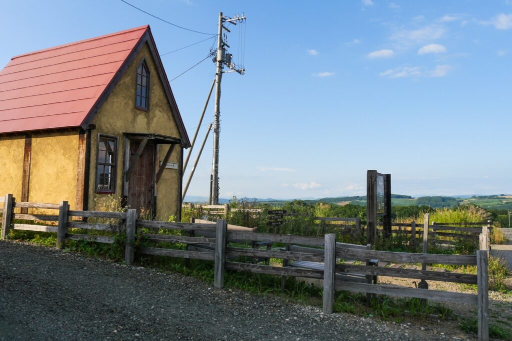 Kleines gelbes Häuschen mit rotem Dach vor blauem Himmel in der ländlichen Region von Hokkaido im Sommer.