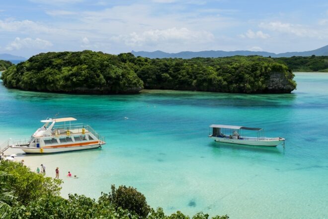 Blick auf das blaue Wasser und die kleinen Inseln der Kabira Bay in Ishigaki. Zwei Boote scheinen auf dem Wasser zu schweben.