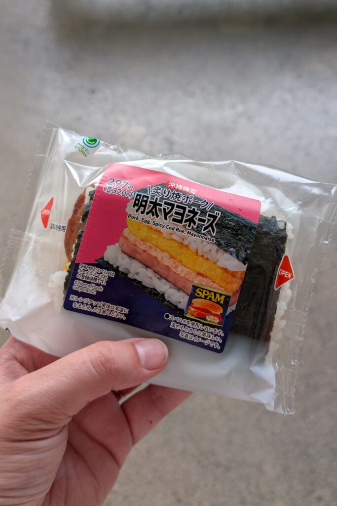 Eine Hand hält Onigiri gefüllt mit Spam in die Kamera.