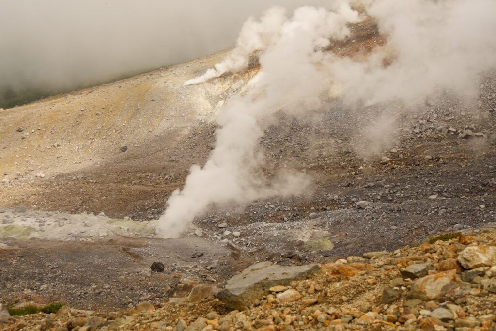 Blick vom Wanderweg zum Gipfel des Mt. Asahidake auf dampfende Fumarole. 