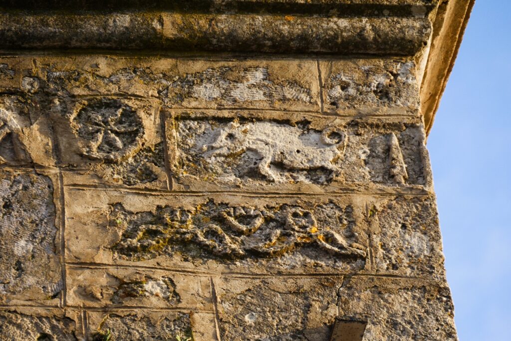 Verwitterter Stein mit eingemeißelten Ornamenten und Tierdarstellungen an einer historischen Mauer