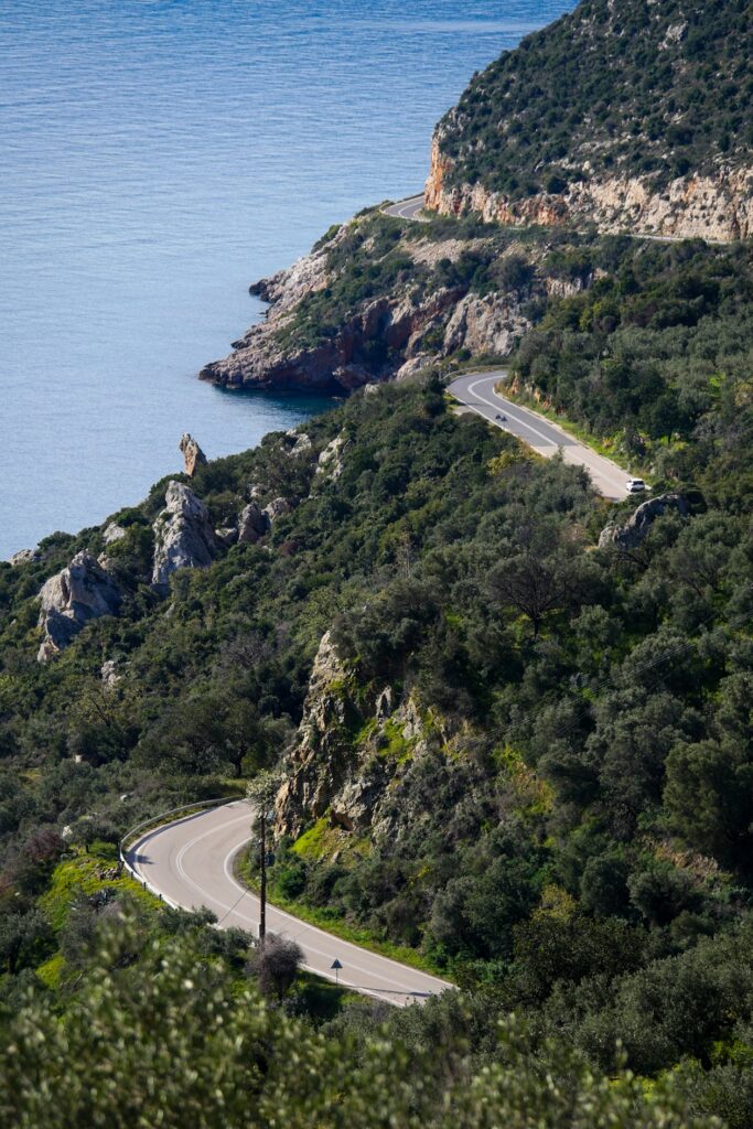 Küstenstraße mit mehreren Kurven entlang bewaldeter Felsen am Meer