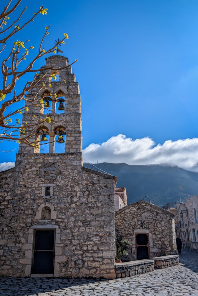 Steinerne Kirche in Areopoli mit Glockenturm vor blauem Himmel und Bergen im Hintergrund