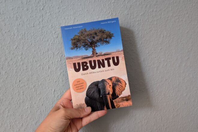 Eine Hand hält das Buch Ubuntu gegen eine hellblaue Wand