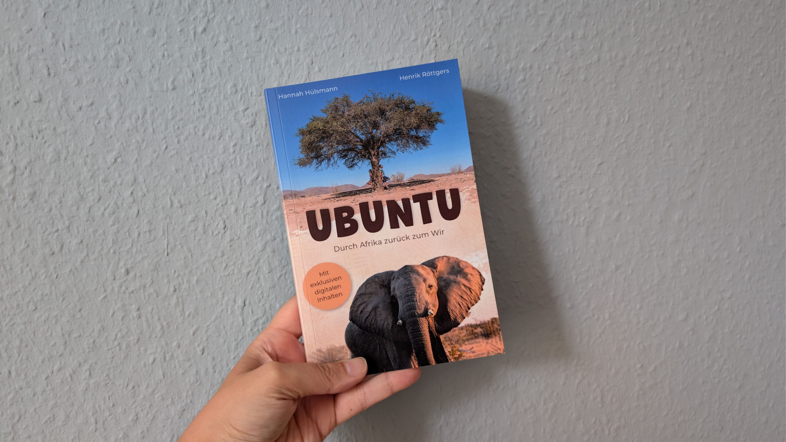 Eine Hand hält das Buch Ubuntu gegen eine hellblaue Wand