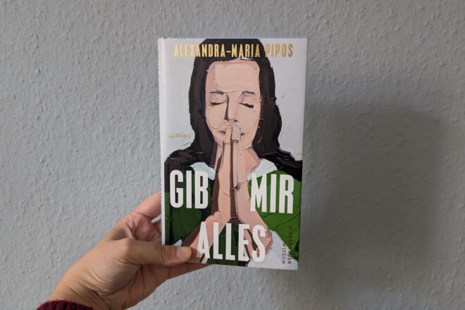 Hand hält Buch mit Titel 'Gib mir alles' und Illustration einer betenden Frau mit geschlossenen Augen vor grauer Wand