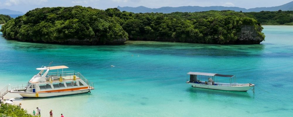 Blick auf das blaue Wasser und die kleinen Inseln der Kabira Bay in Ishigaki. Zwei Boote scheinen auf dem Wasser zu schweben.